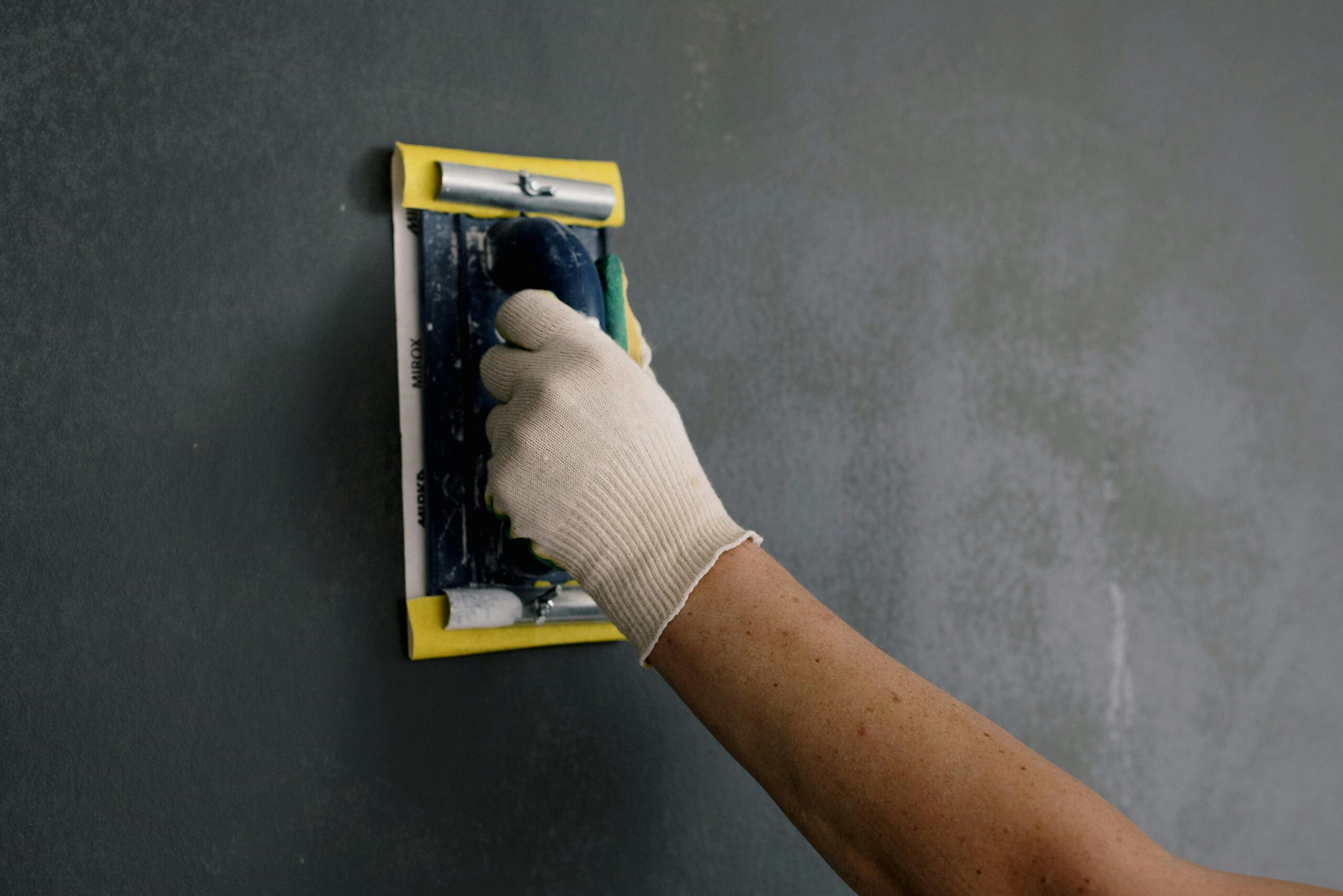 Close-up of a hand smoothing a wall with a spackle tool during home renovation.